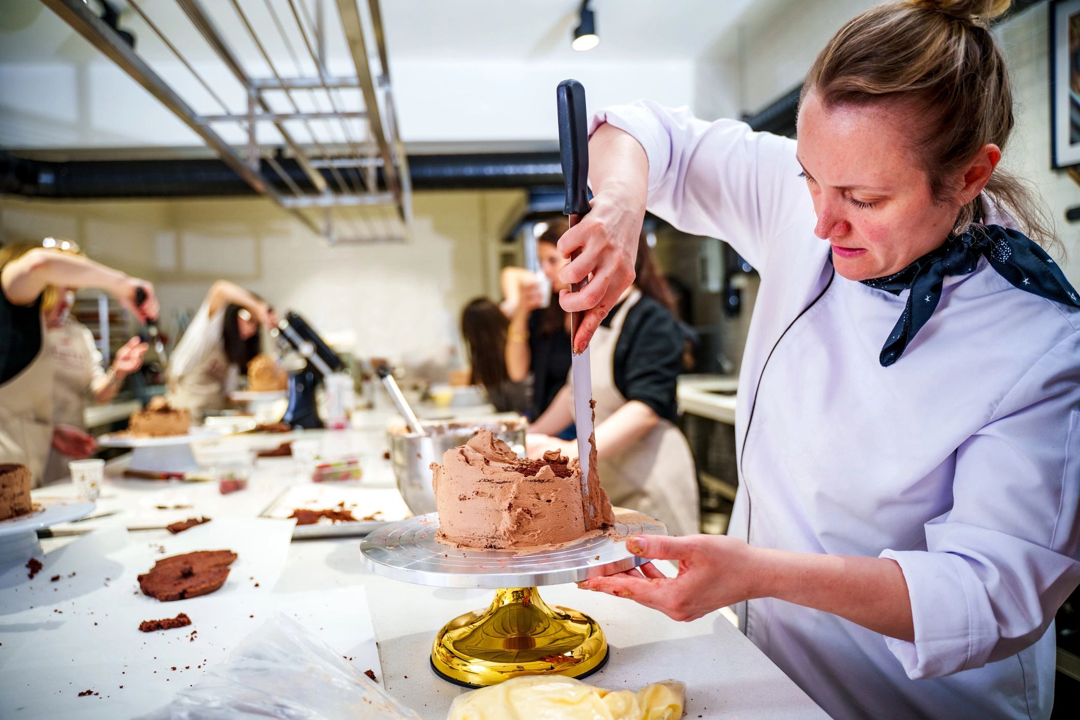 Pastry chef frosting a layered cake in a bakery kitchen